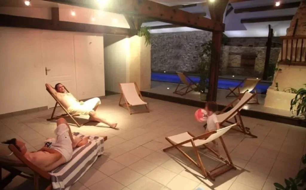 Piscine intérieure chauffée et privée avec transats en bois, murs en pierre apparente