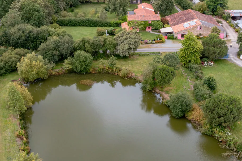 Vue aérienne du gîte au bord de l'étang privé, entouré de prairies et de haies bocagères