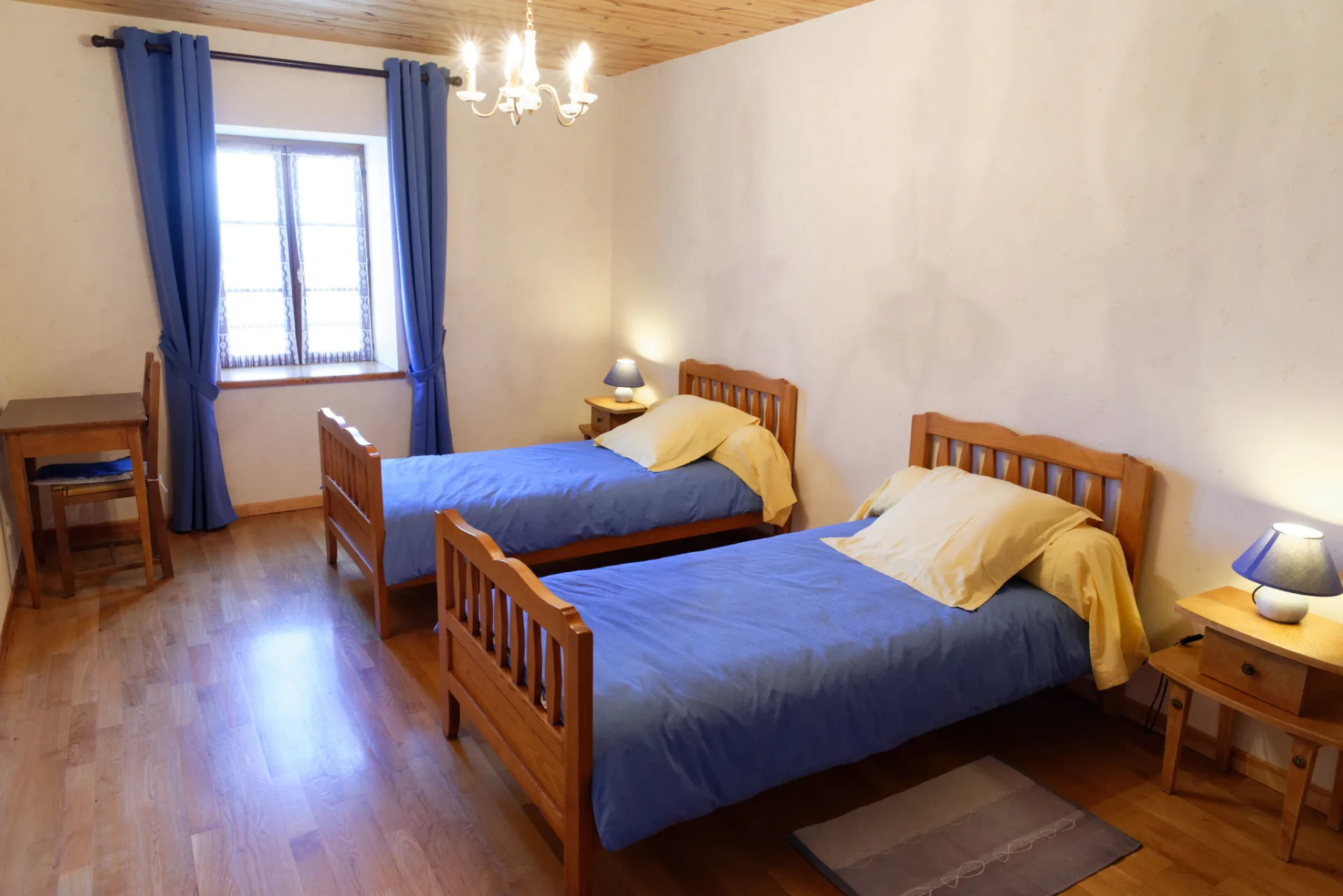 Chambre avec deux lits jumeaux à parure bleue et poutres au plafond