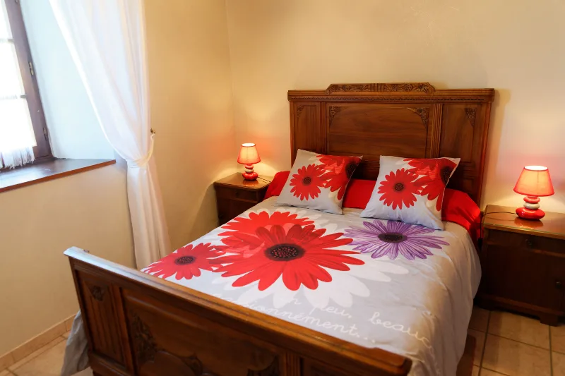 Chambre avec lit double, tête de lit en bois sculpté et parure fleurie rouge