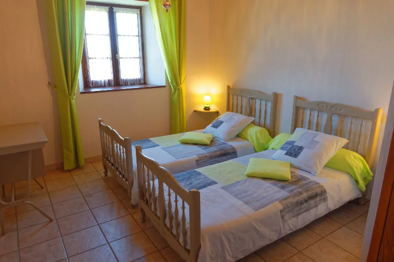 Chambre avec deux lits jumeaux et rideaux vert anis, ambiance lumineuse