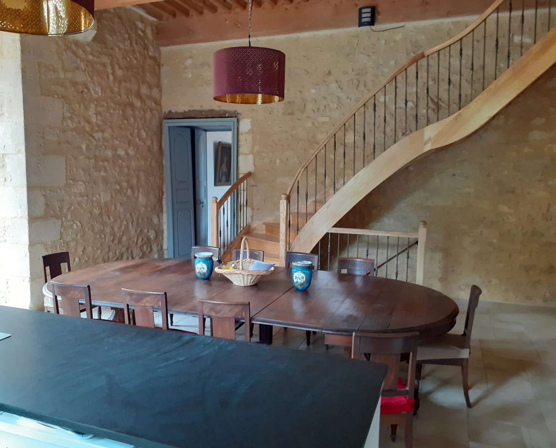 Salle avec grande table ronde en bois et escalier en bois menant à l'étage