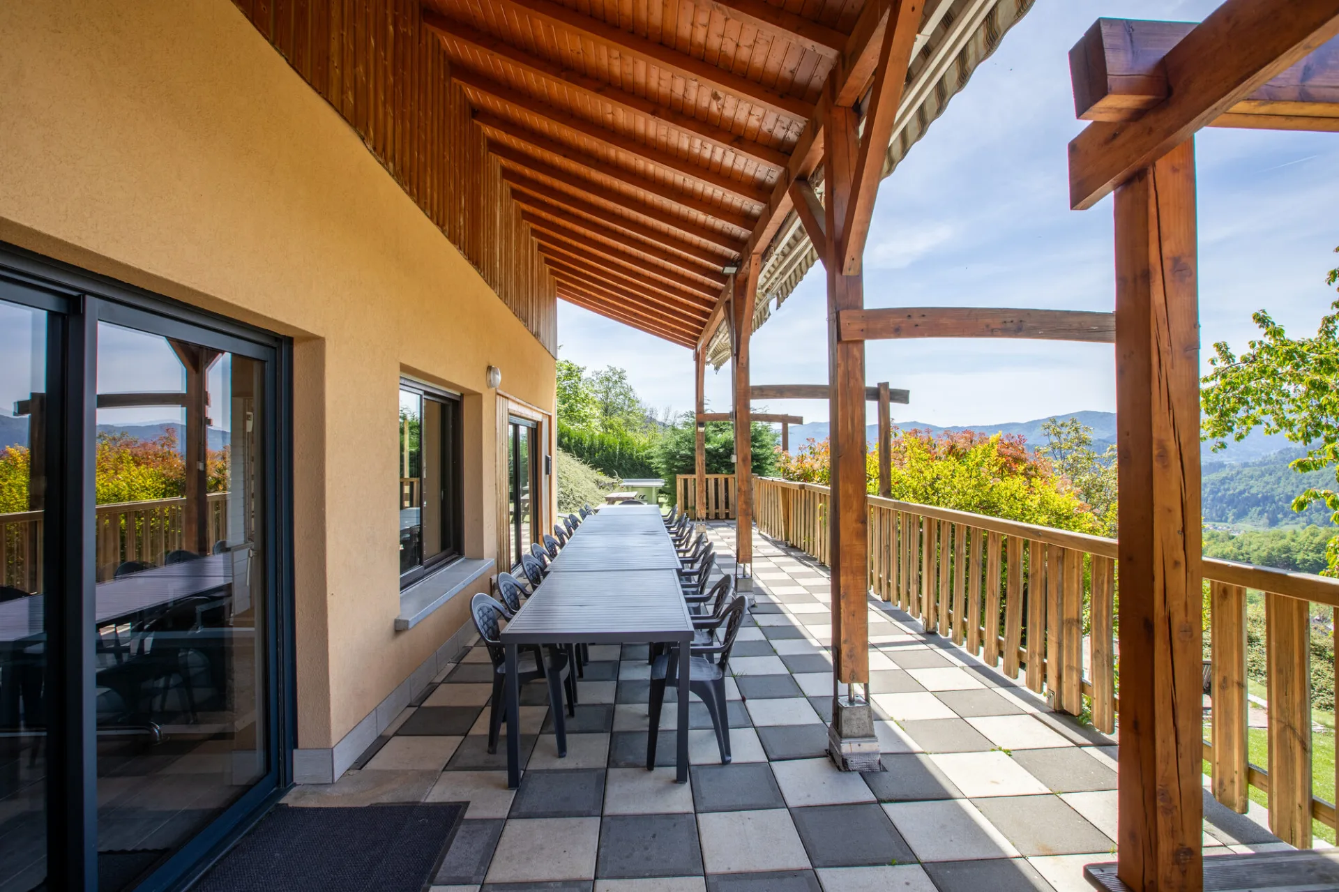 Terrasse couverte sous pergola en bois avec longue table dressée et vue sur les Vosges