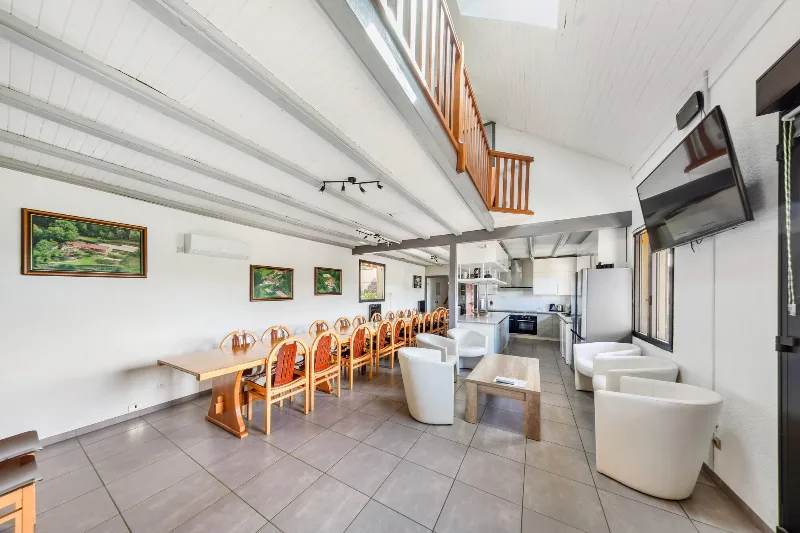 Grand séjour avec longue table conviviale, mezzanine bois et cuisine ouverte en fond