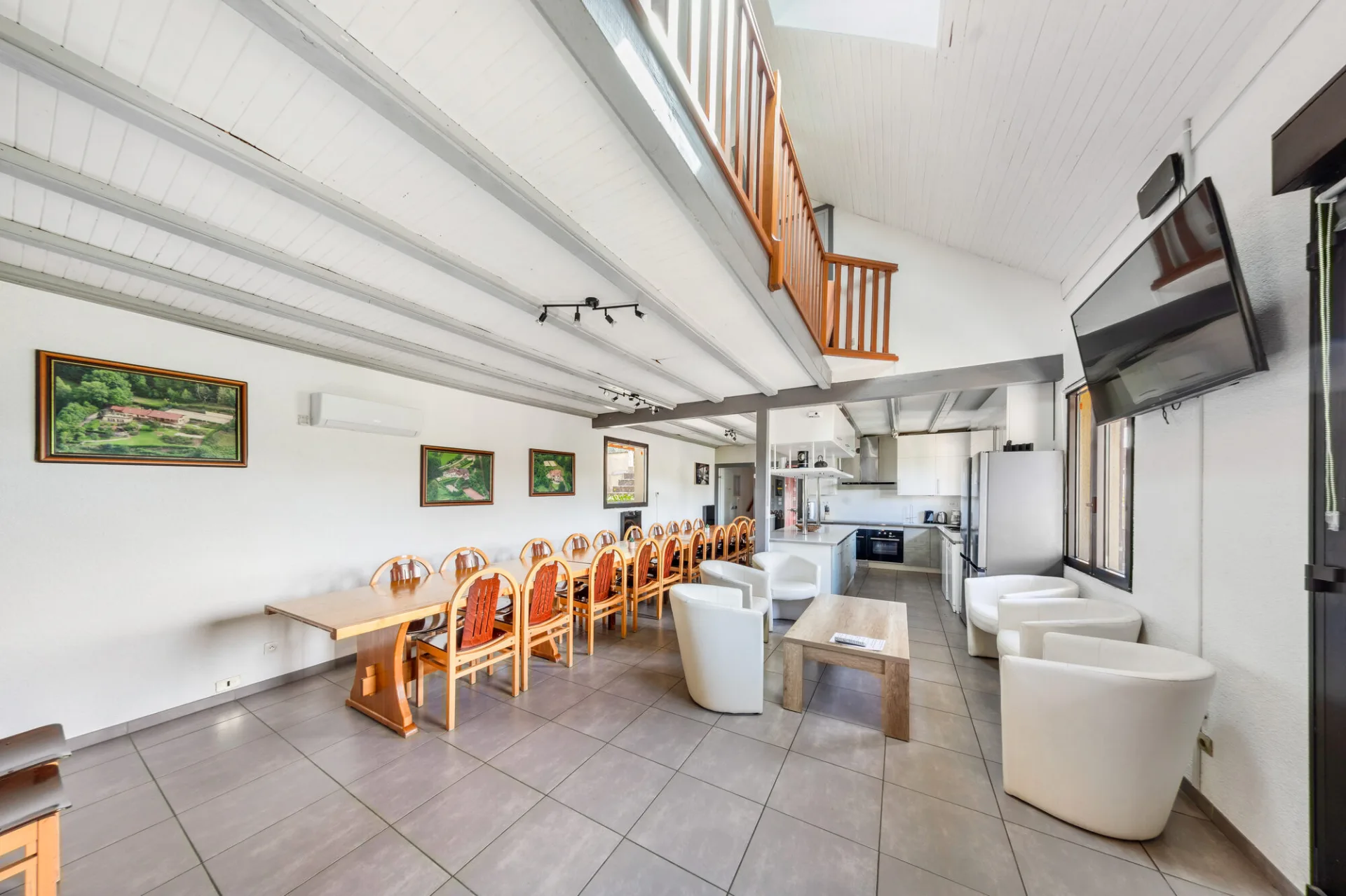Grand séjour avec longue table conviviale, mezzanine bois et cuisine ouverte en fond