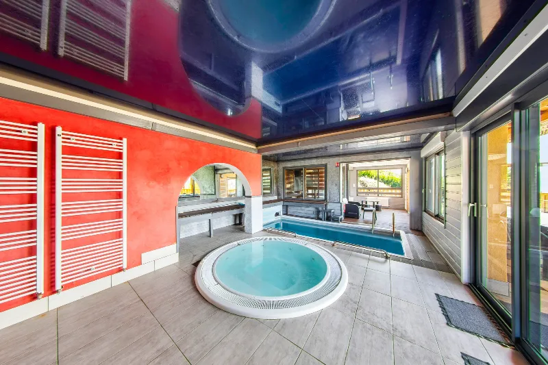 Piscine couverte et spa jacuzzi aux reflets rouge et bleu, espace bien-être privatif