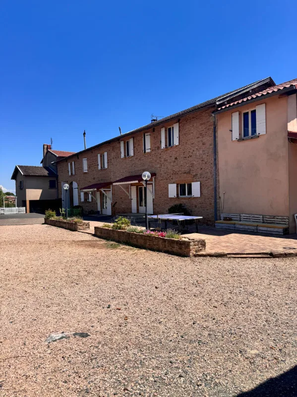 Façade en pierre dorée typique du Beaujolais, longue bâtisse sous ciel bleu avec volets blancs