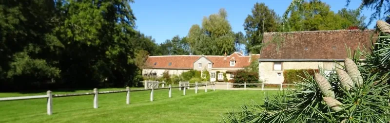 Façade en pierre du gîte vue depuis le pré avec clôture en bois et toiture en tuiles