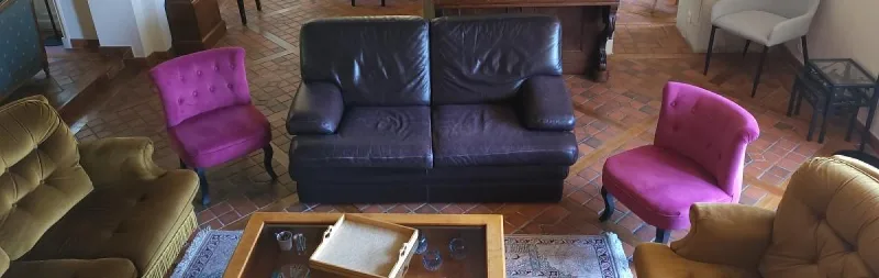 Salon avec canapé en cuir et fauteuils roses vus en plongée sur un sol en tomettes anciennes