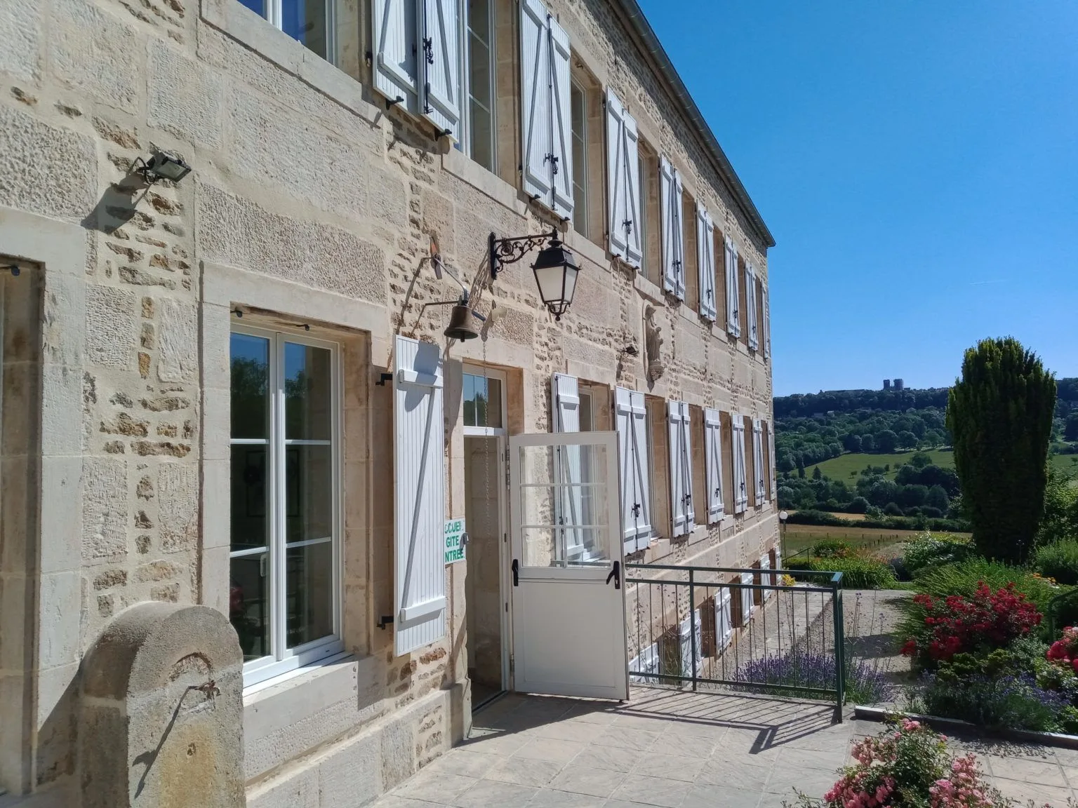 Gîte de groupe Ferme Sainte-Anne à Langres — Façade en pierre de la Ferme Sainte-Anne avec volets blancs et vue sur la campagne de Langres, capacité 30 personnes