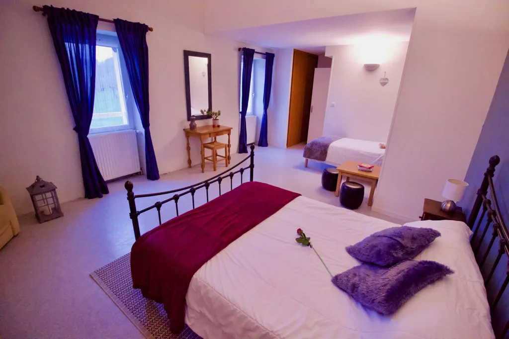 Chambre avec lit en fer forgé et linge de lit prune