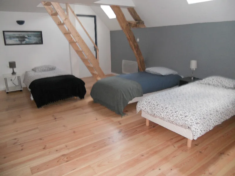 Chambre avec trois lits simples et escalier en bois menant à l'étage