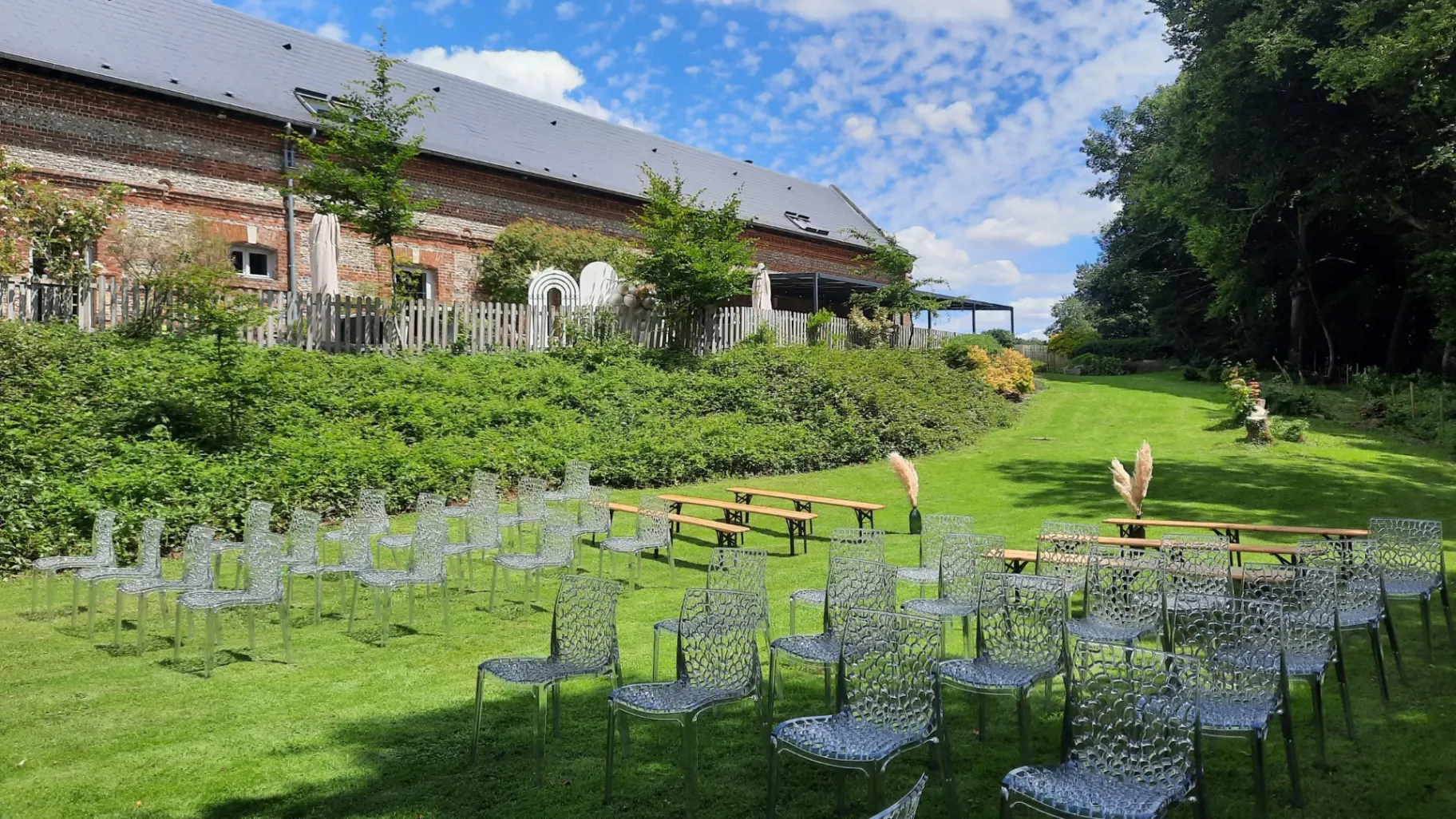 Jardin arboré avec chaises de cérémonie installées sur la pelouse face à la longère