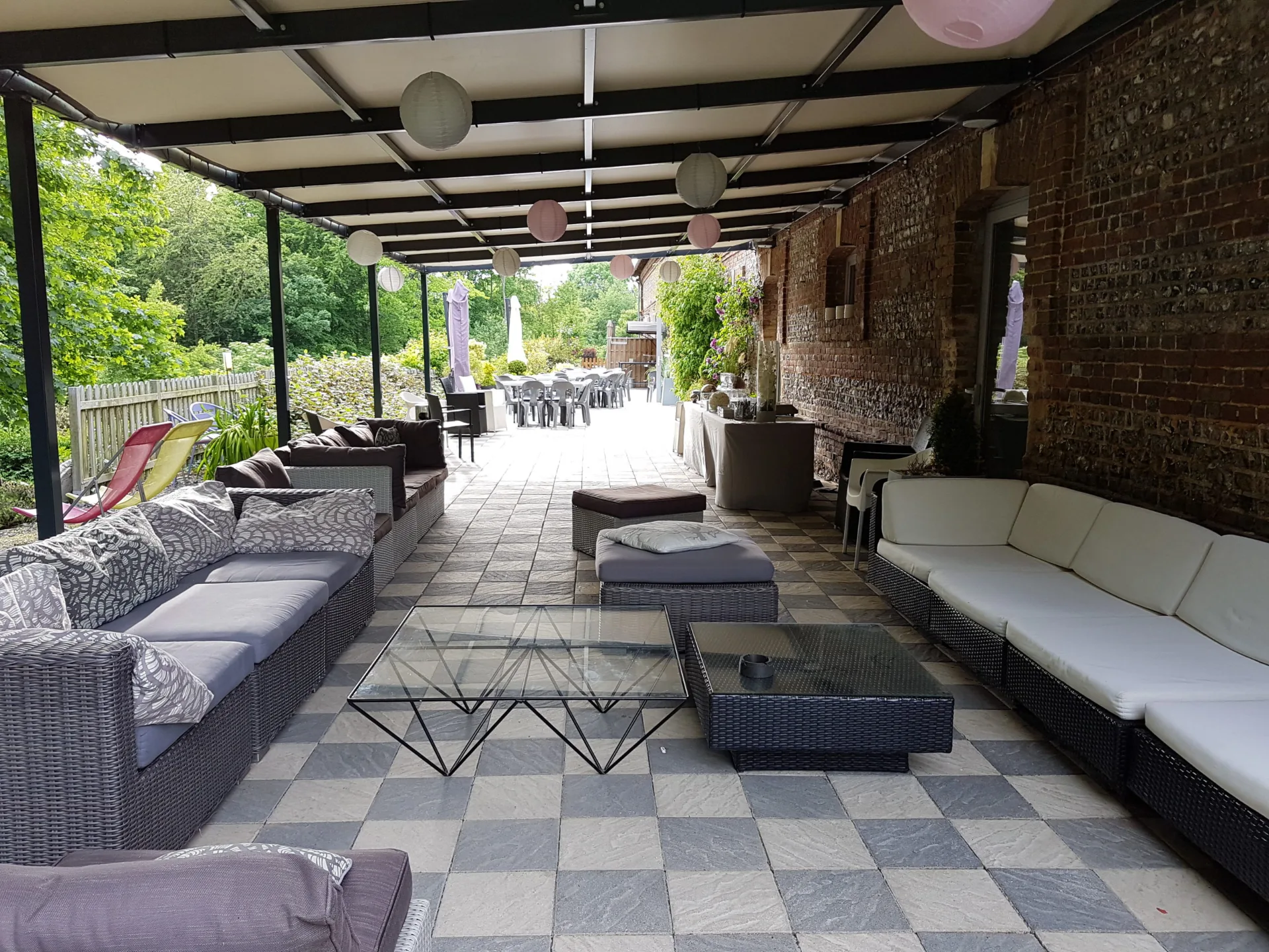 Salon extérieur couvert avec canapés en résine tressée et lampions colorés