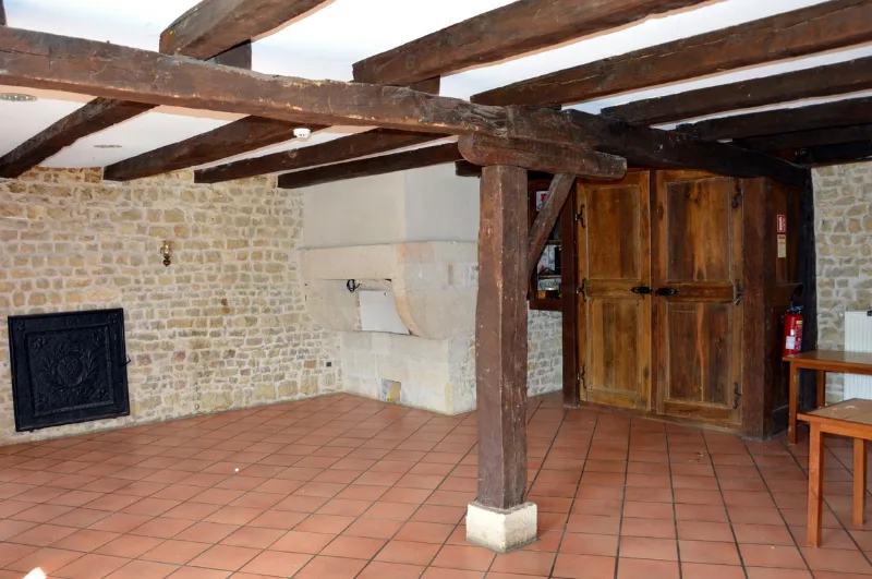 Grande salle avec cheminée en pierre et poutres apparentes, idéale pour les repas de groupe
