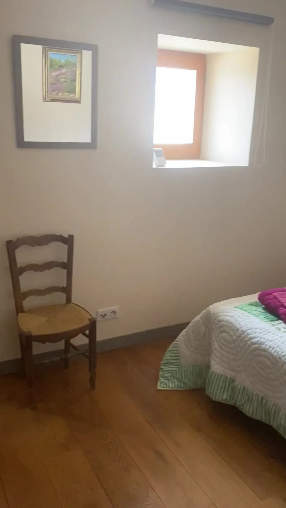 Chambre lumineuse avec tableau, chaise en bois et fenêtre en pierre