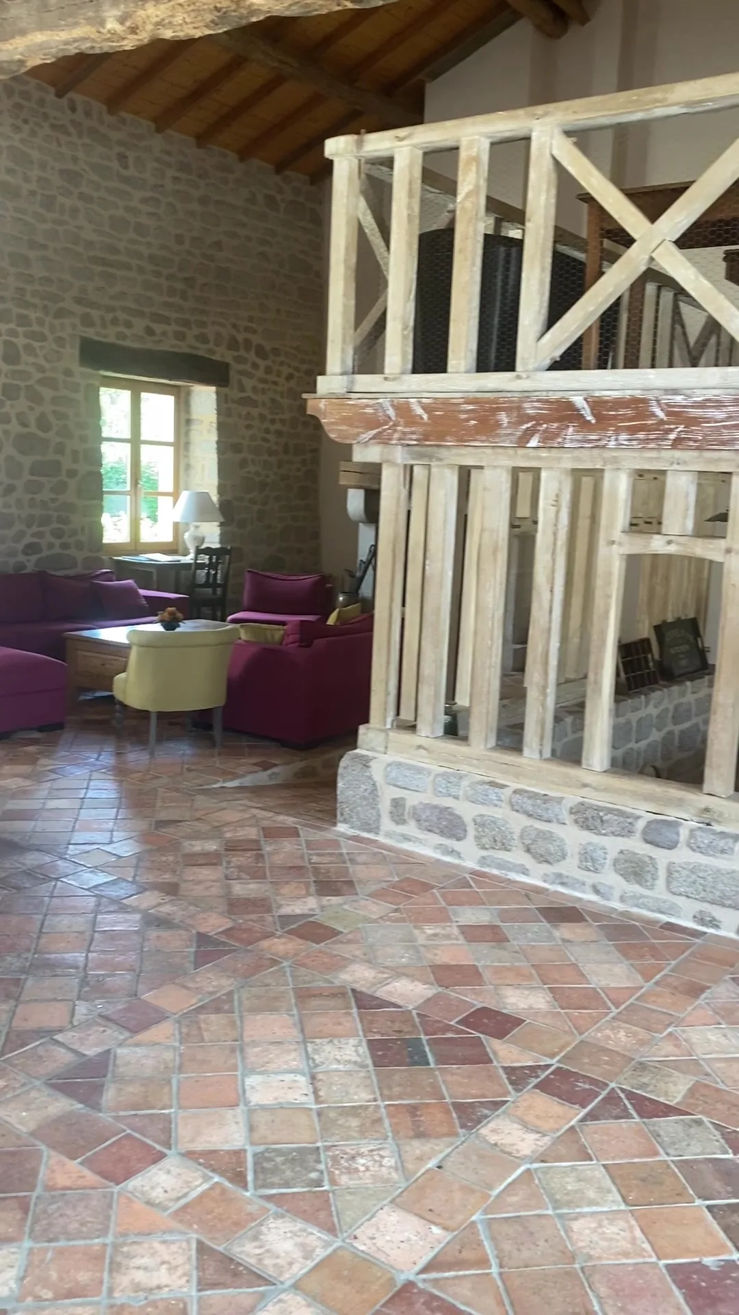 Grand salon avec fauteuils bordeaux, cheminée en pierre et poutres apparentes