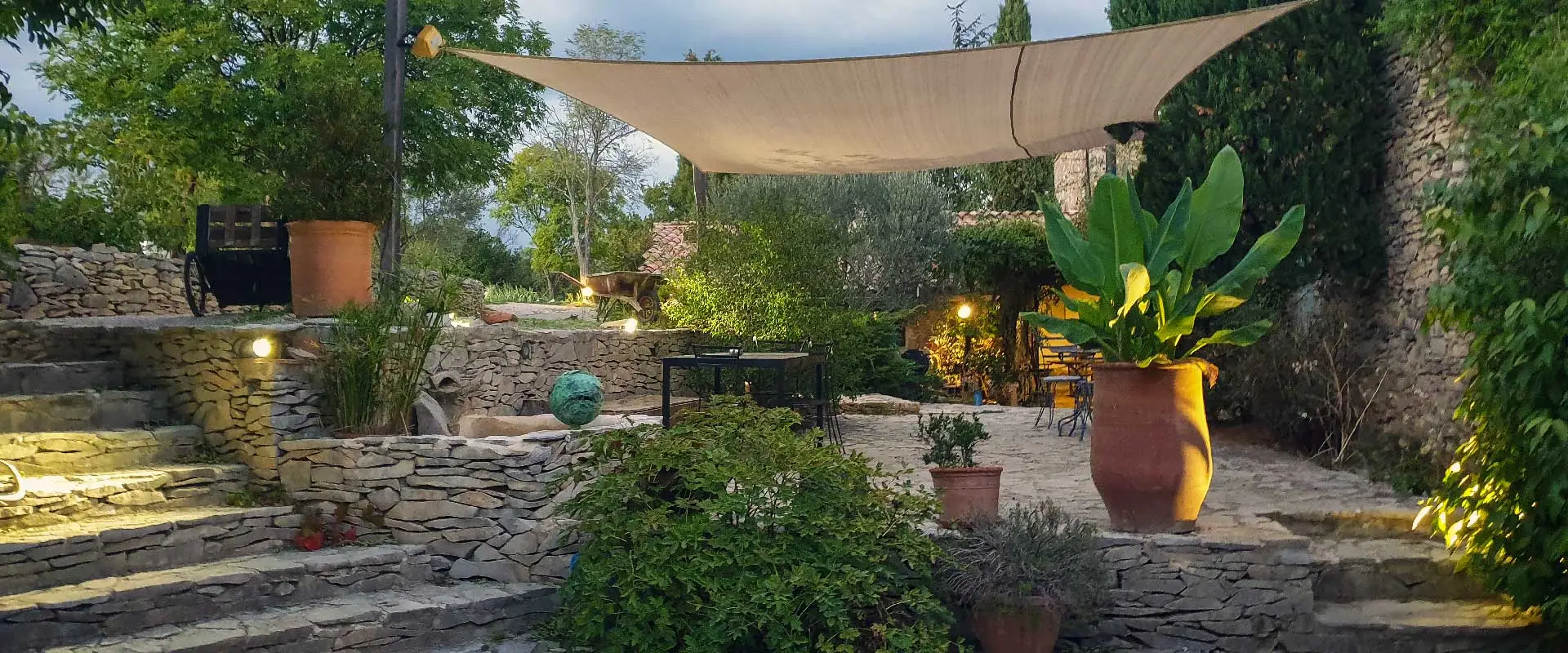 Terrasse en pierre éclairée avec voile d'ombrage et mobilier de jardin