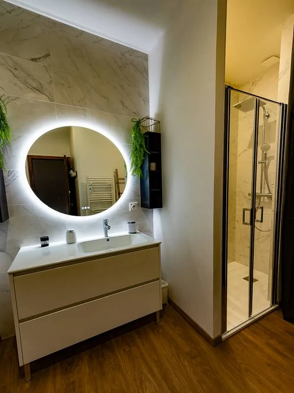 Salle d'eau moderne avec vasque, miroir lumineux rond et douche à l'italienne