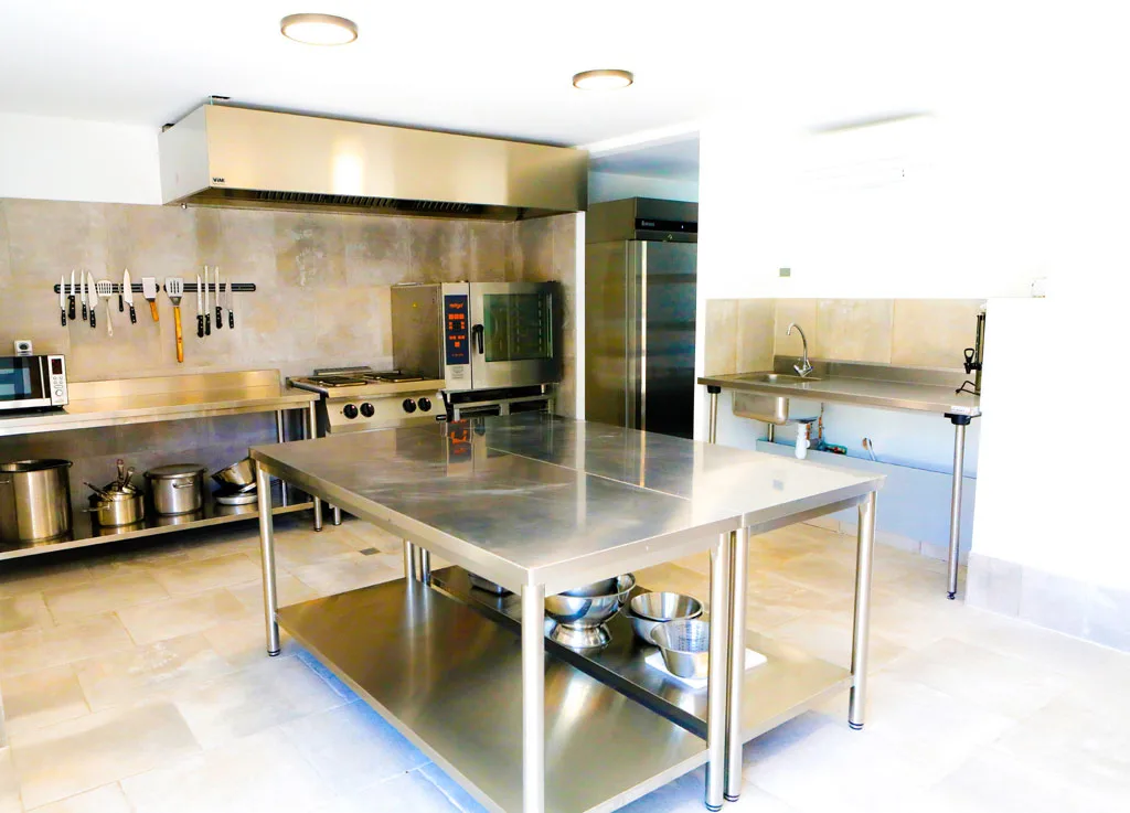 Cuisine professionnelle équipée d'un piano de cuisson, d'une desserte inox et d'un grand réfrigérateur
