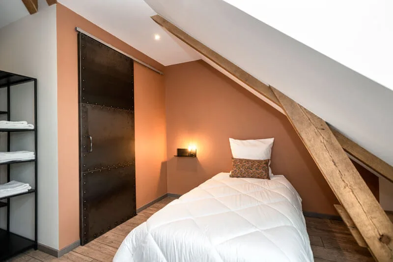 Chambre lumineuse avec lit simple, porte coulissante ancienne et murs terracotta