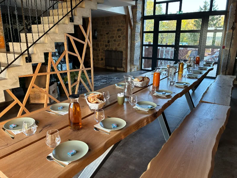 Grande table conviviale en bois brut dressée pour un repas de groupe, avec verrière sur le paysage