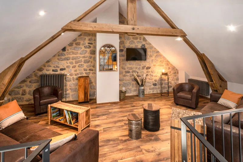 Mezzanine salon avec charpente en bois apparente, fauteuils en cuir et coin lecture