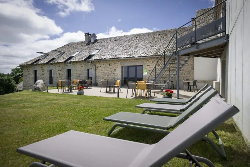 Terrasse en pierre avec mobilier extérieur et transats face à la façade en pierre du gîte