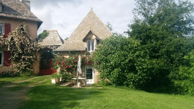 Façade en pierre du domaine du Cayla avec toiture pointue et roses grimpantes