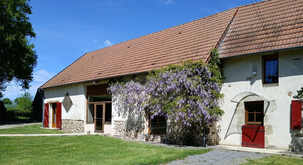 Vue extérieure de la longère en pierre avec glycine en fleurs sur la façade