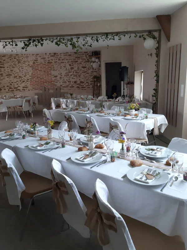 Salle de réception aménagée façon champêtre avec nappes blanches et fleurs des champs