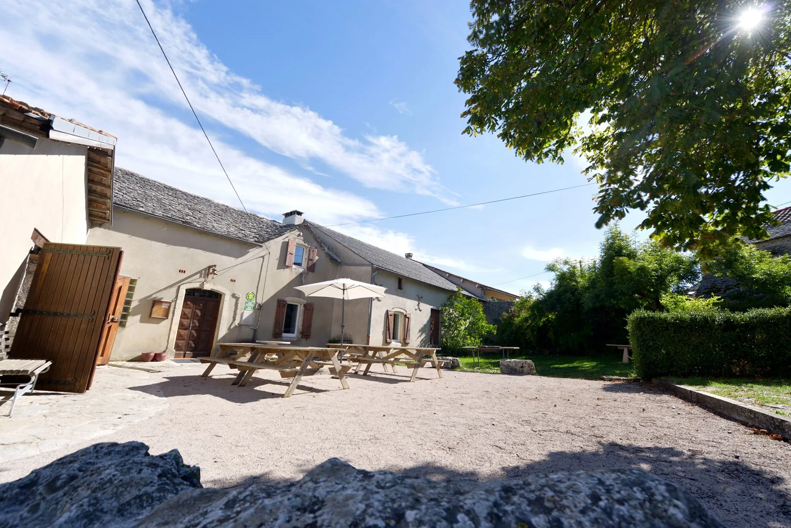 Cour intérieure avec tables de pique-nique en bois et façade en pierre du gîte
