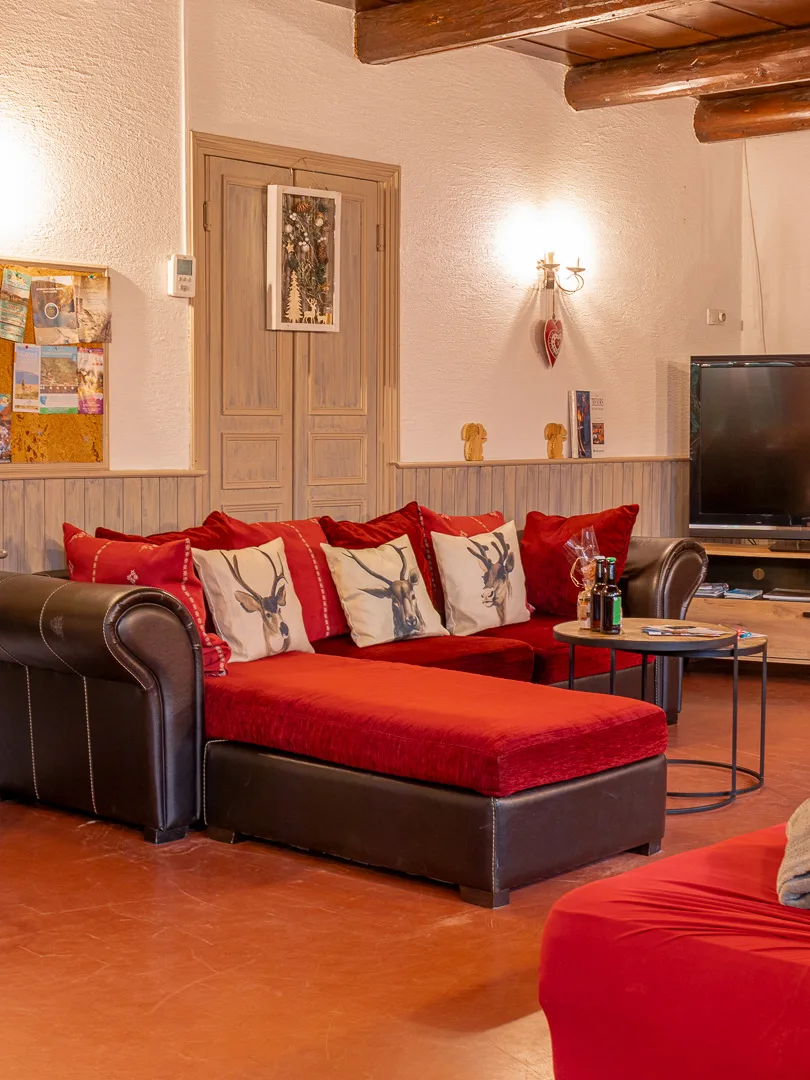 Salon chaleureux avec canapé en cuir rouge, coussins à motifs cerfs et télévision