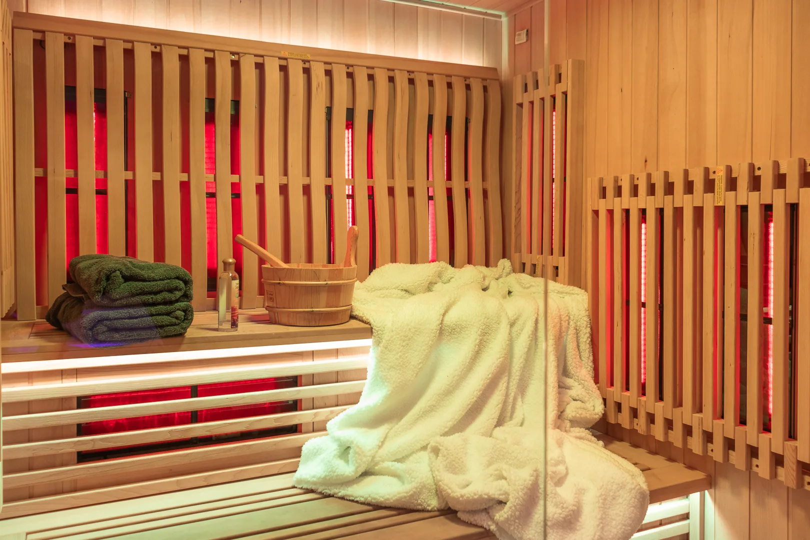 Sauna infrarouge avec bancs en bois, seau et serviettes moelleuses