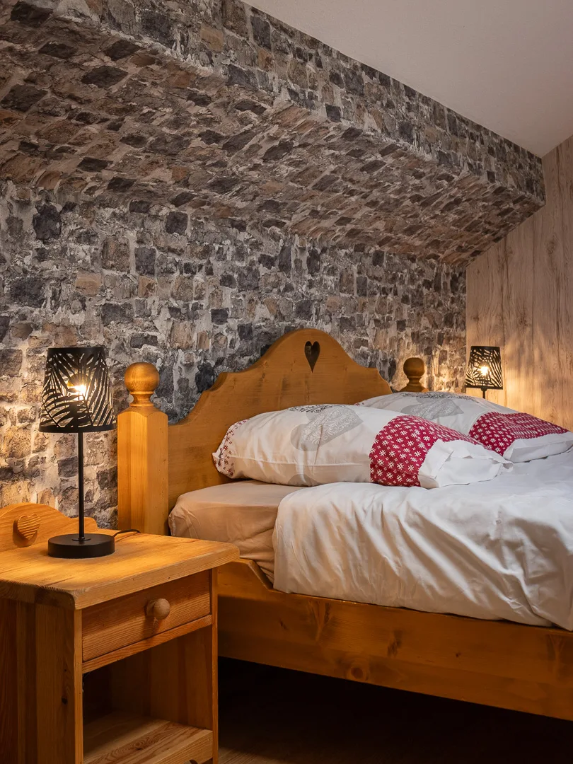 Chambre voûtée en pierre avec tête de lit en bois sculpté et lampes chevet
