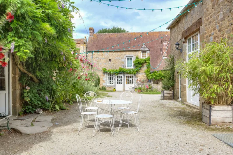 Terrasse fleurie avec tables et chaises devant la façade en pierre couverte de glycine