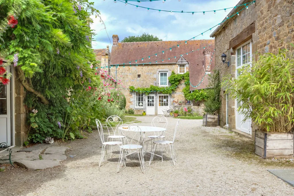 Terrasse fleurie avec tables et chaises devant la façade en pierre couverte de glycine