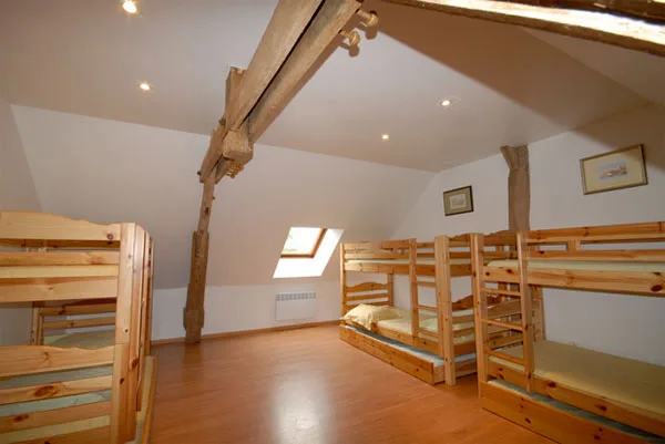 Dortoir sous combles avec plusieurs lits superposés en bois