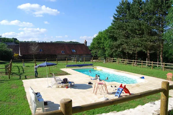 Piscine extérieure entourée de pelouse et de barrières en bois, vue dégagée sur les arbres