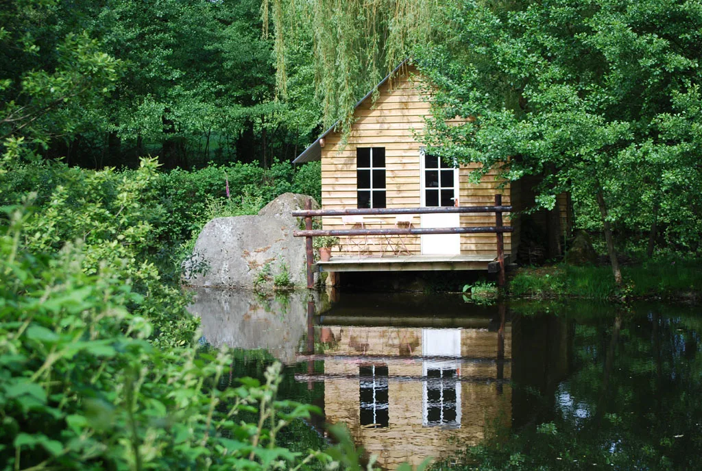 Cabane en bois sur pilotis au bord de l'étang, entourée d'arbres
