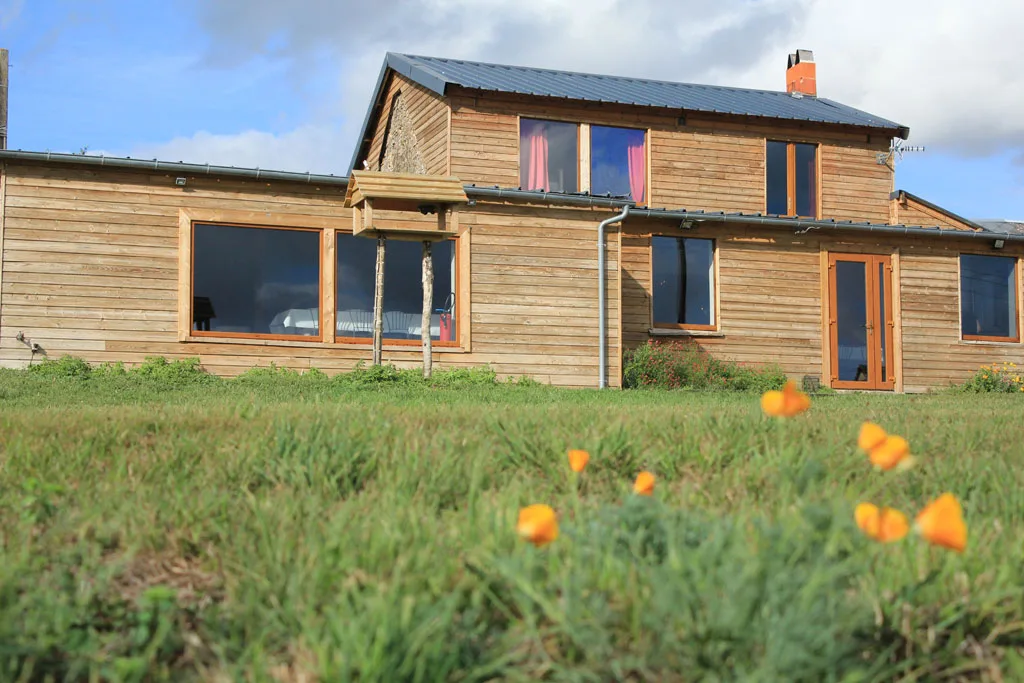 Gîte de groupe Ferme de la Poterie à Saint-Denis-d'Orques — Façade en bois moderne de la maison principale avec grande baie vitrée et toit en zinc, capacité 80 personnes