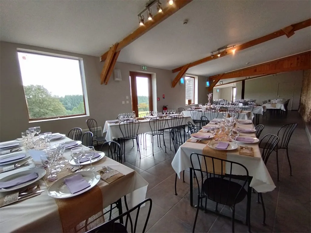 Salle à manger lumineuse avec poutres apparentes et tables dressées devant de grandes fenêtres