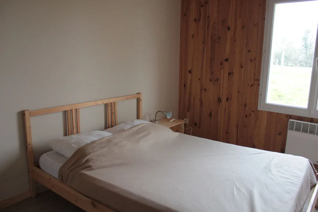Chambre avec lit double en bois clair et vue sur la campagne