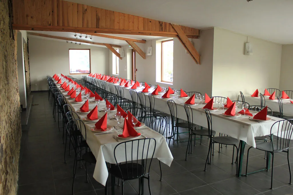Grande salle de réception dressée avec longues tables blanches et serviettes rouges pliées