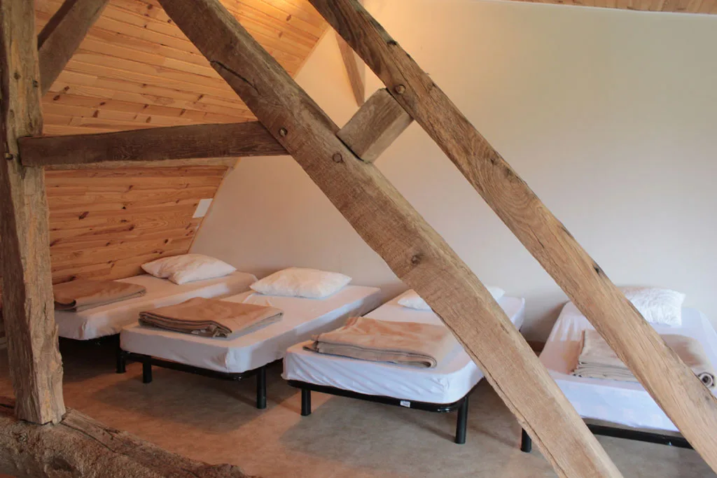 Dortoir sous combles avec plusieurs lits simples et couvertures pliées