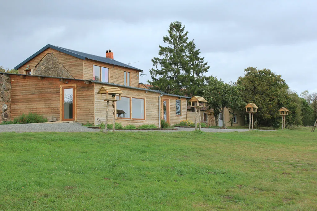 Vue d'ensemble de la façade en bois et pierre du gîte, entourée de prairie