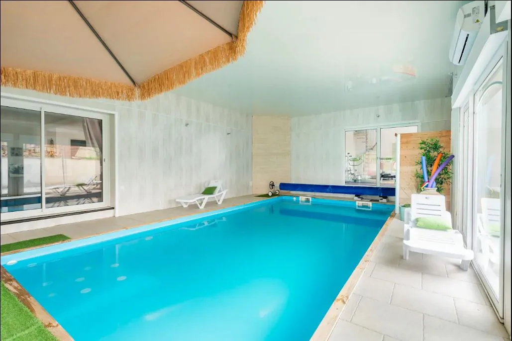 Piscine intérieure chauffée avec transats et grandes baies vitrées
