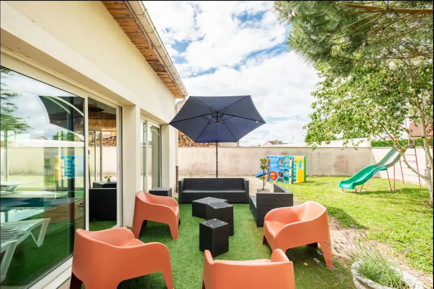 Terrasse extérieure couverte avec salon de jardin, vue sur la pelouse et les jeux d'enfants