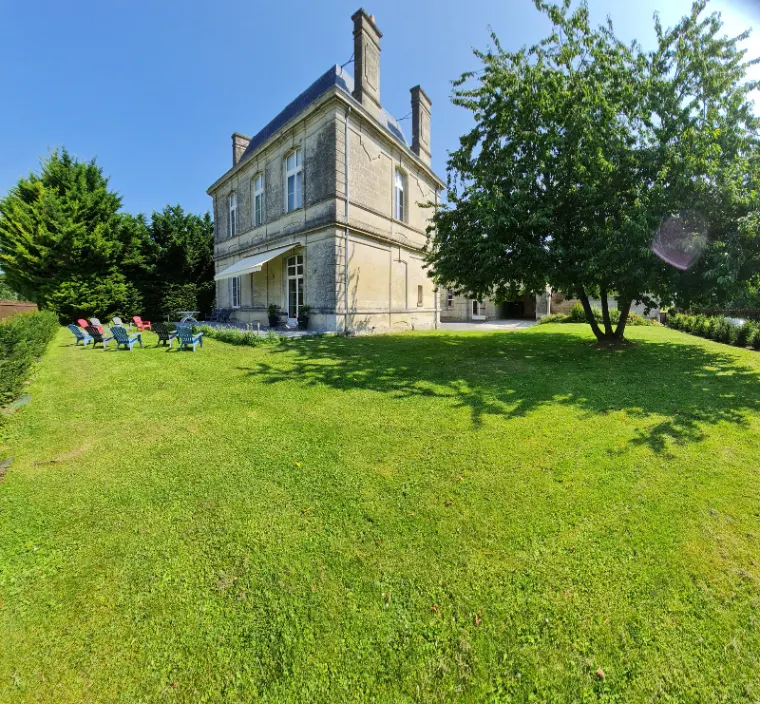 Vue arrière de la maison en pierre avec pelouse et transats colorés