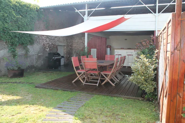 Terrasse en bois avec grande table et chaises rouges sous voile d'ombrage